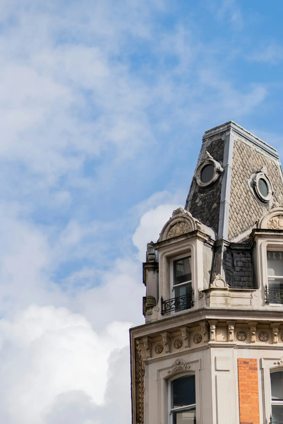 An ornate mansard roofline with dormer and oeil-de-boeuf windows against open sky