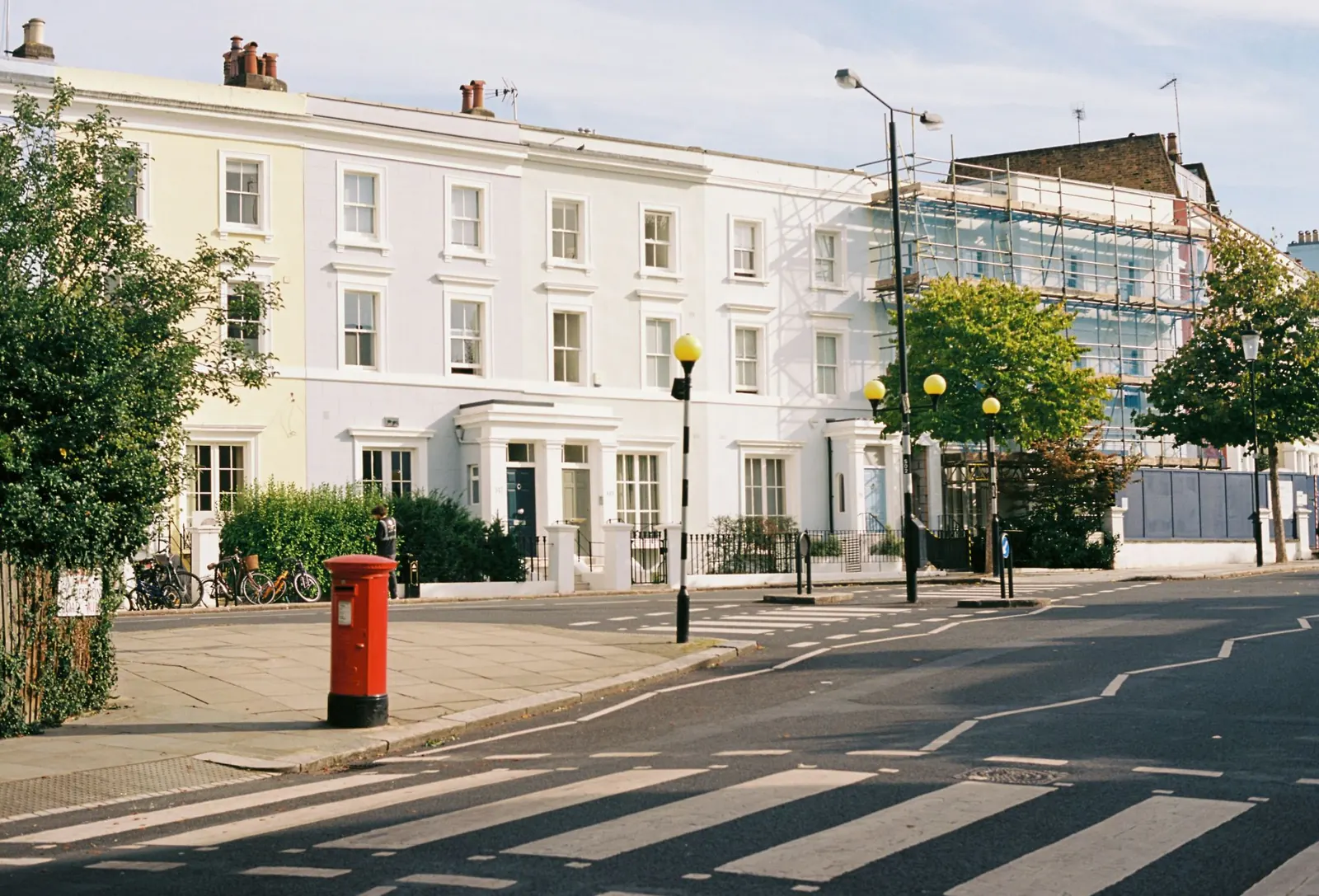A pastel stuccoed terrace of three storeys with timber sash windows and columned doorcases, seen across the street on a bright autumn morning