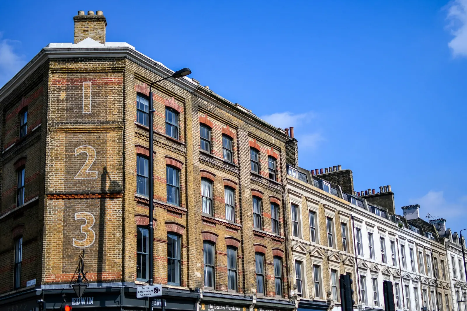 A stock brick corner building of three storeys with sash windows and red brick dressings, a stuccoed terrace running away beside it